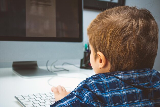 Photo rear view of boy using computer while sitting at home