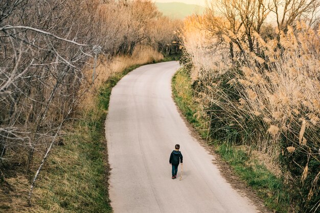 Photo rear view of boy walking on road amidst trees