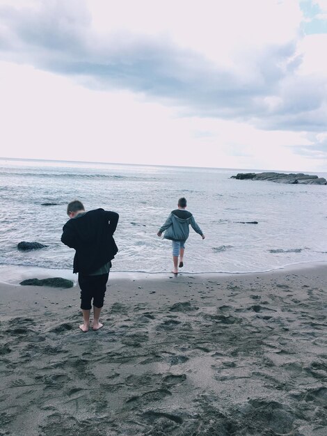 Foto vista posteriore di ragazzi sulla spiaggia contro un cielo nuvoloso