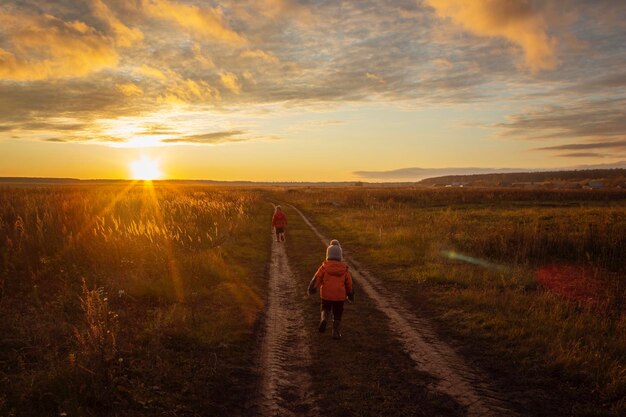 Rear view of boys on field against sky during sunset