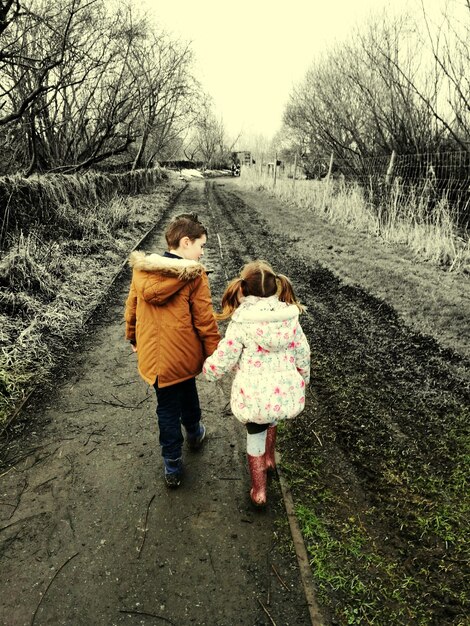 Photo rear view of brother and sister walking on footpath during winter