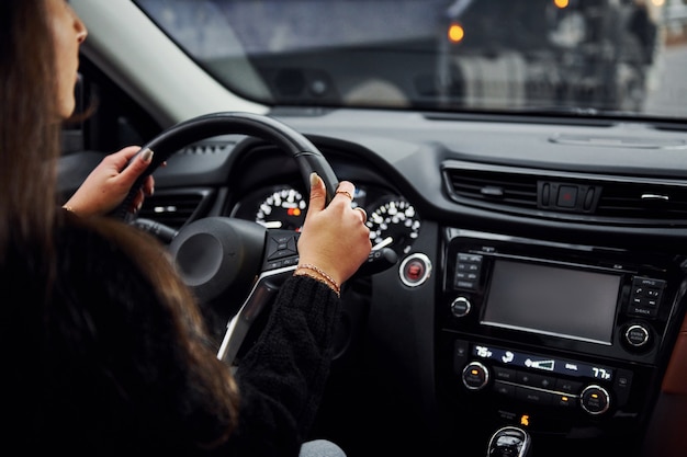 Rear view of brunette female driver that riding modern car at daytime.