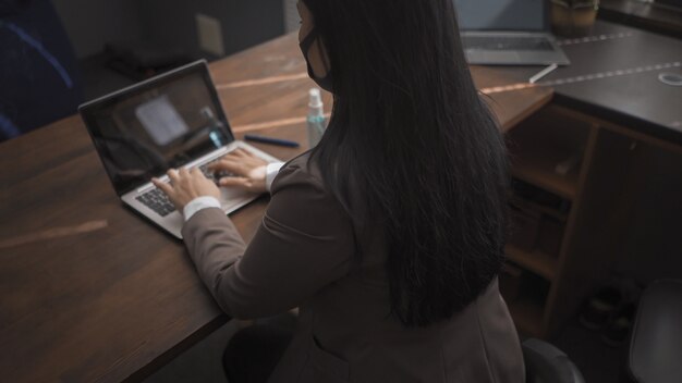 Rear view of Brunette in medical mask types on computer