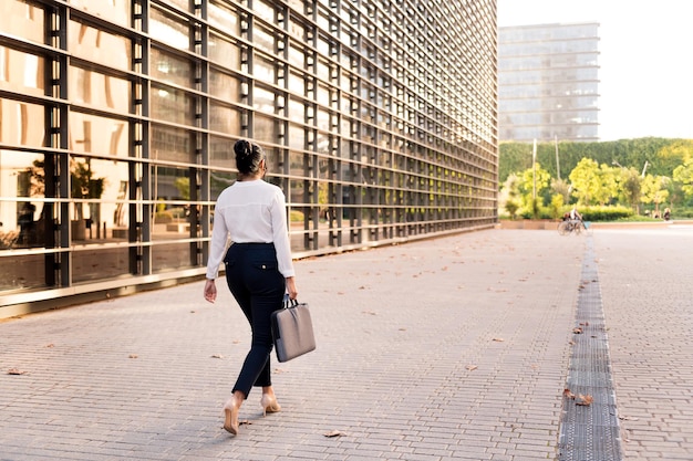 Photo rear view of a business woman walking by the financial district of the city, concept of successful entrepreneur and urban lifestyle, copy space for text