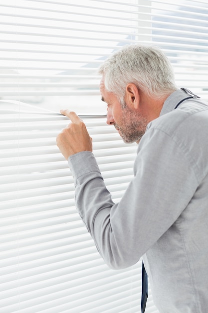 Rear view of a businessman peeking through blinds