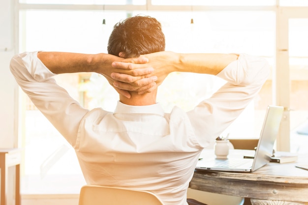 Rear view of businessman sitting on chair with his hands on head