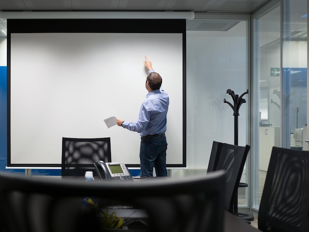 Photo rear view of businessman standing by projection screen in board room at office