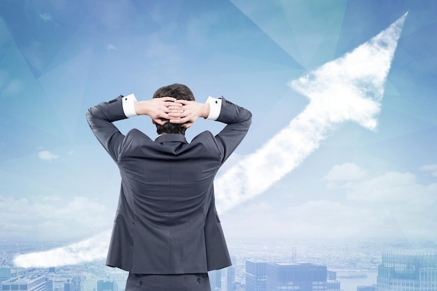 Rear view of a businessman standing with his hands behind his head and looking at a growing graph in a city sky