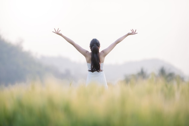 rear view of carefree woman with arms raised standing on field against sky