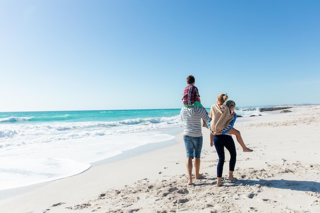 Rear view of a Caucasian family on the beach with blue sky and sea in the background, walking and piggybacking