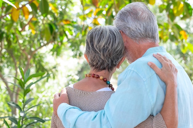 Rear view of Caucasian senior couple walking in the woods tenderly embraced expressing love and care Two mature adult grandparents enjoy a healthy lifestyle in the public park