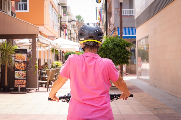 Rear view of caucasian senior cyclist woman running with electric bicycle in a city street Elderly active lady enjoying a healthy lifestyle using sustainable mobility