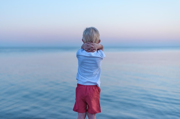 일몰과 바다 배경에서 아이의 후면보기 어린이 외로움 개념