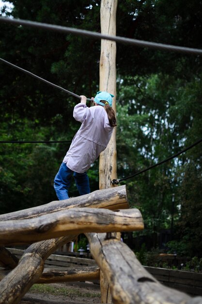 Rear view of a child who spends time without gadgets, having fun climbing in a tourist rope park.