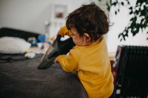 Photo rear view of child with vacuum cleaner at home