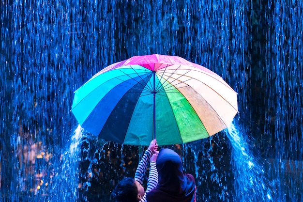 Photo rear view of children holding umbrella under rain during night