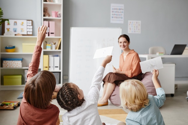 Vista posteriore dei bambini che mostrano le carte all'insegnante mentre sono seduti a lezione a scuola