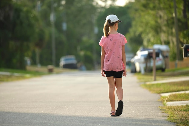 Rear view of confident young child girl walking along the sunny alley Active lifestyle on summer holidays