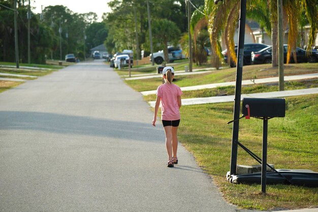 Rear view of confident young child girl walking along the sunny alley Active lifestyle on summer holidays