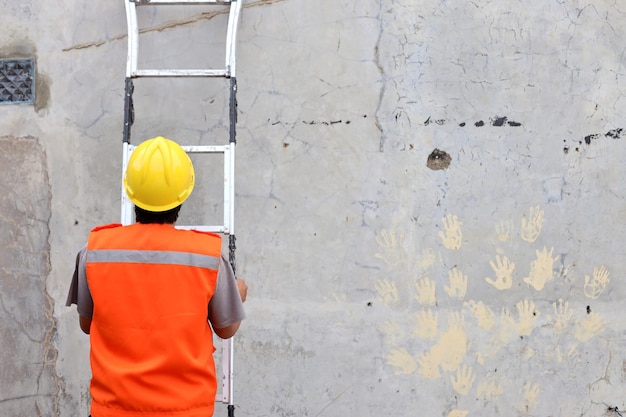 Rear view of construction worker holding aluminum ladder and leaning it on building wall Copy space