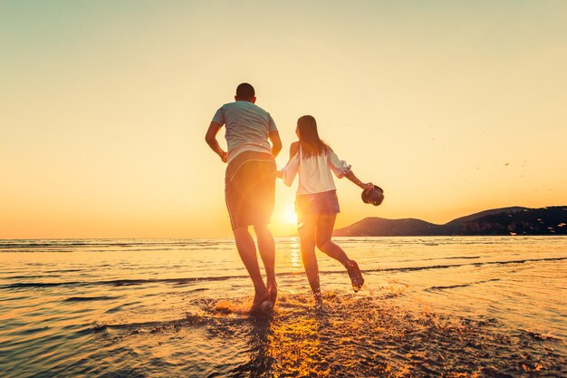 Rear view of couple on beach against sky during sunset