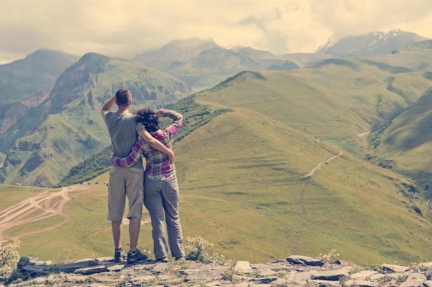 Rear view couple hikers looking into the distance is standing on the top of mountain Background is mountains valley and cloudy sky