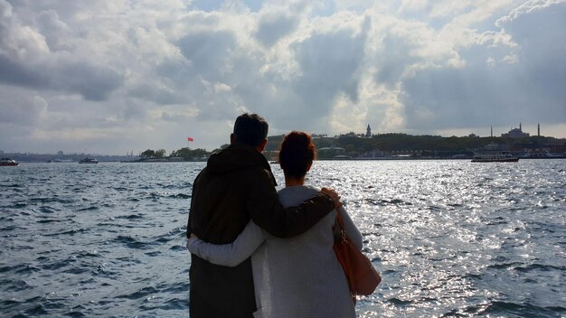 Rear view of couple looking at sea against cloudy sky