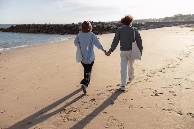 rear view of couple in love is walk holding hands across the sunny beach