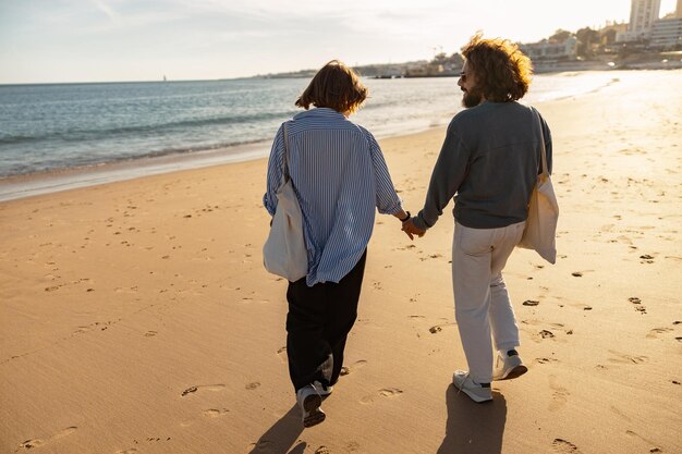 rear view of couple in love is walk holding hands across the sunny beach