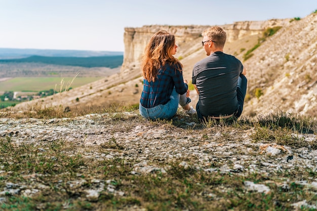 Rear view of couple in love a man and a woman sit on the edge of a cliff overlooking the cliff