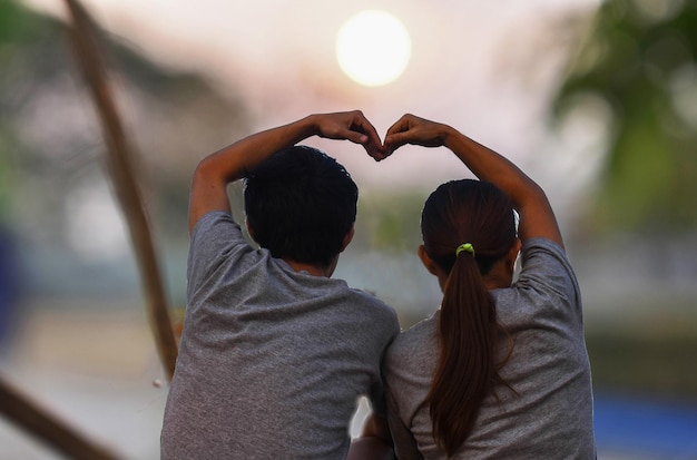 Photo rear view of couple making heart shape while sitting outdoors