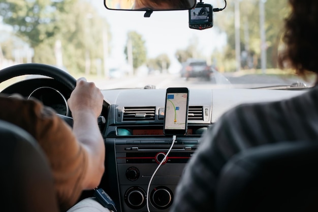 Rear view of a couple of people driving a car using a map navigator mobile app Selective focus on smartphone screen inside car interior