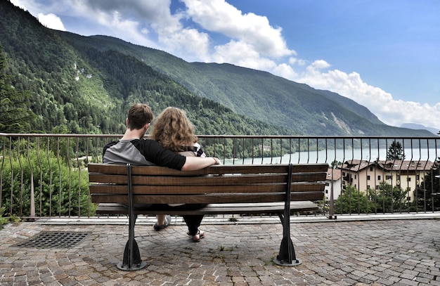 Rear view of couple sitting on bench against mountains