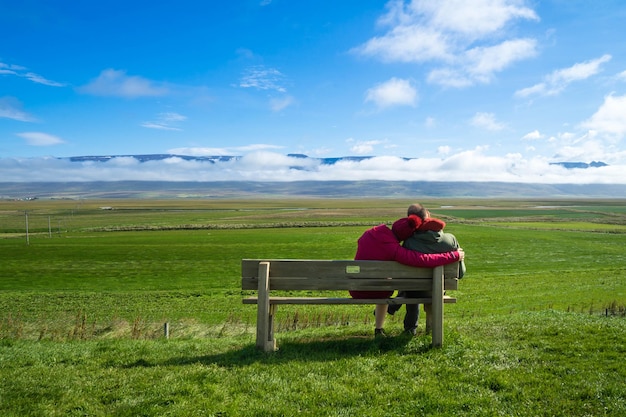 Rear view of couple sitting on bench over landscape against sky