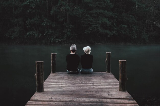 Задний вид пары, сидящей у озера на пирсе