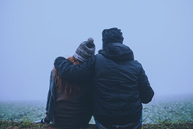 Rear view of couple sitting on land against clear sky during winter