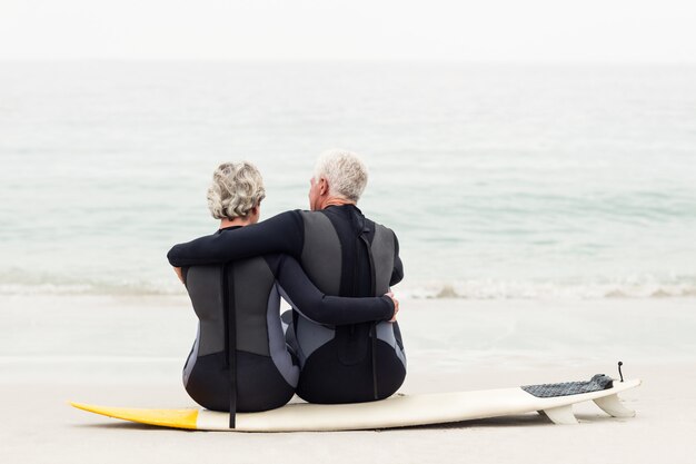 Rear view of couple sitting on surfboard 