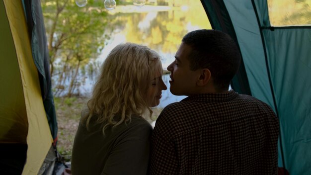 Rear view of couple sitting in tent near the beautiful river lake