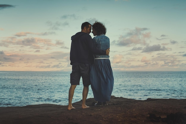 Rear view of couple standing at beach against sky during sunset