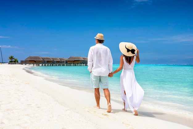 青い空を背景にビーチで歩いているカップルの後ろの景色