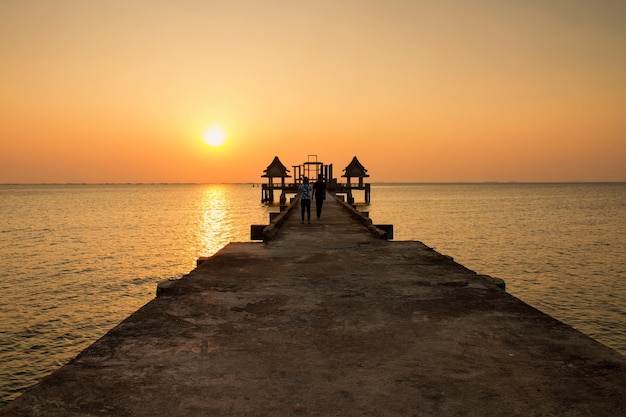 Rear view of couple walking on pier over sea against clear sky during sunset