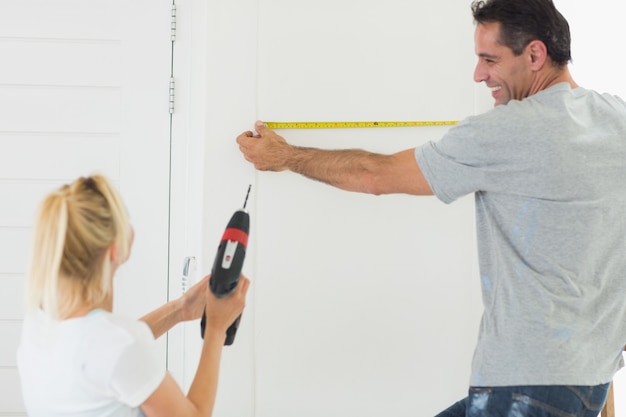 Rear view of a couple with drill and tape at new home