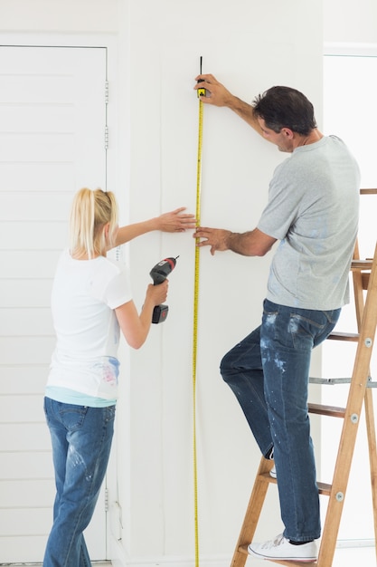 Rear view of a couple with drill and tape at new home