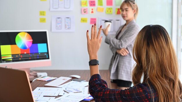 Photo rear view of creative woman raised hand up for asking question during designer team meeting