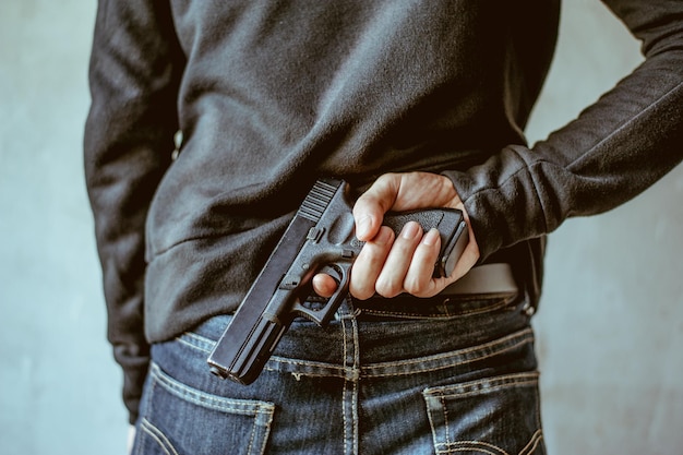 Photo rear view of criminal with handgun standing against wall