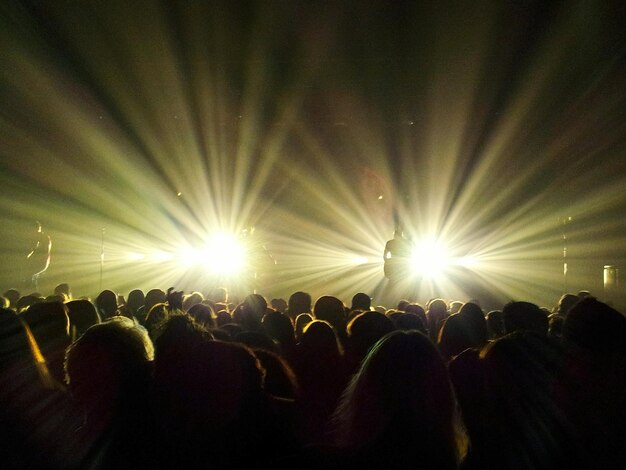 Foto vista posteriore della folla al concerto musicale contro un raggio di luce illuminato