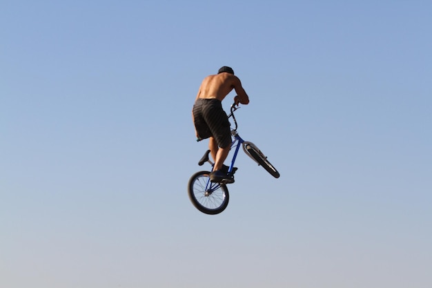 Photo rear view of cyclist performing stunt in mid-air against clear blue sky