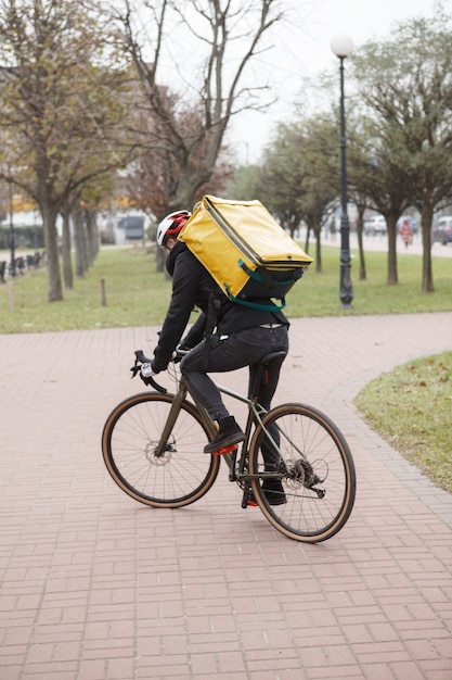 Vista posteriore di un fattorino con zaino termico in bicicletta durante il lavoro