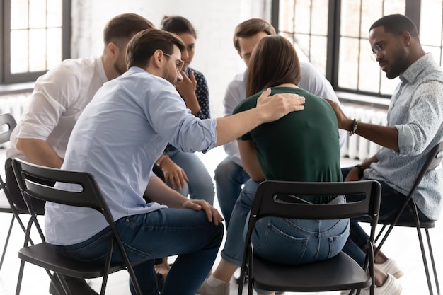 Rear view diverse people supporting frustrated upset woman feeling pain sitting in circle at group counselling therapy session psychological help addictions or depression treatment