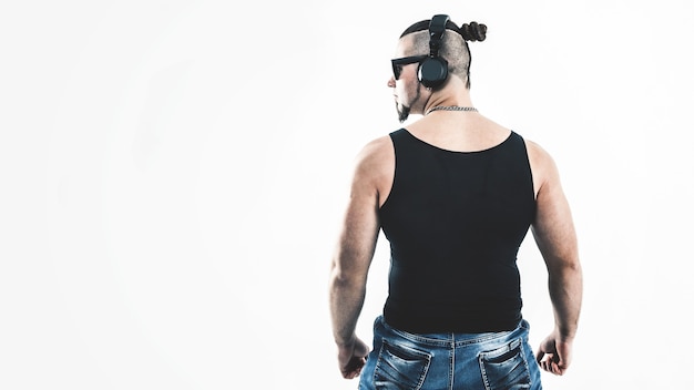 Rear view - DJ - rapper with a stylish hairstyle with headphones on a light wall.the photo has a empty space for your text